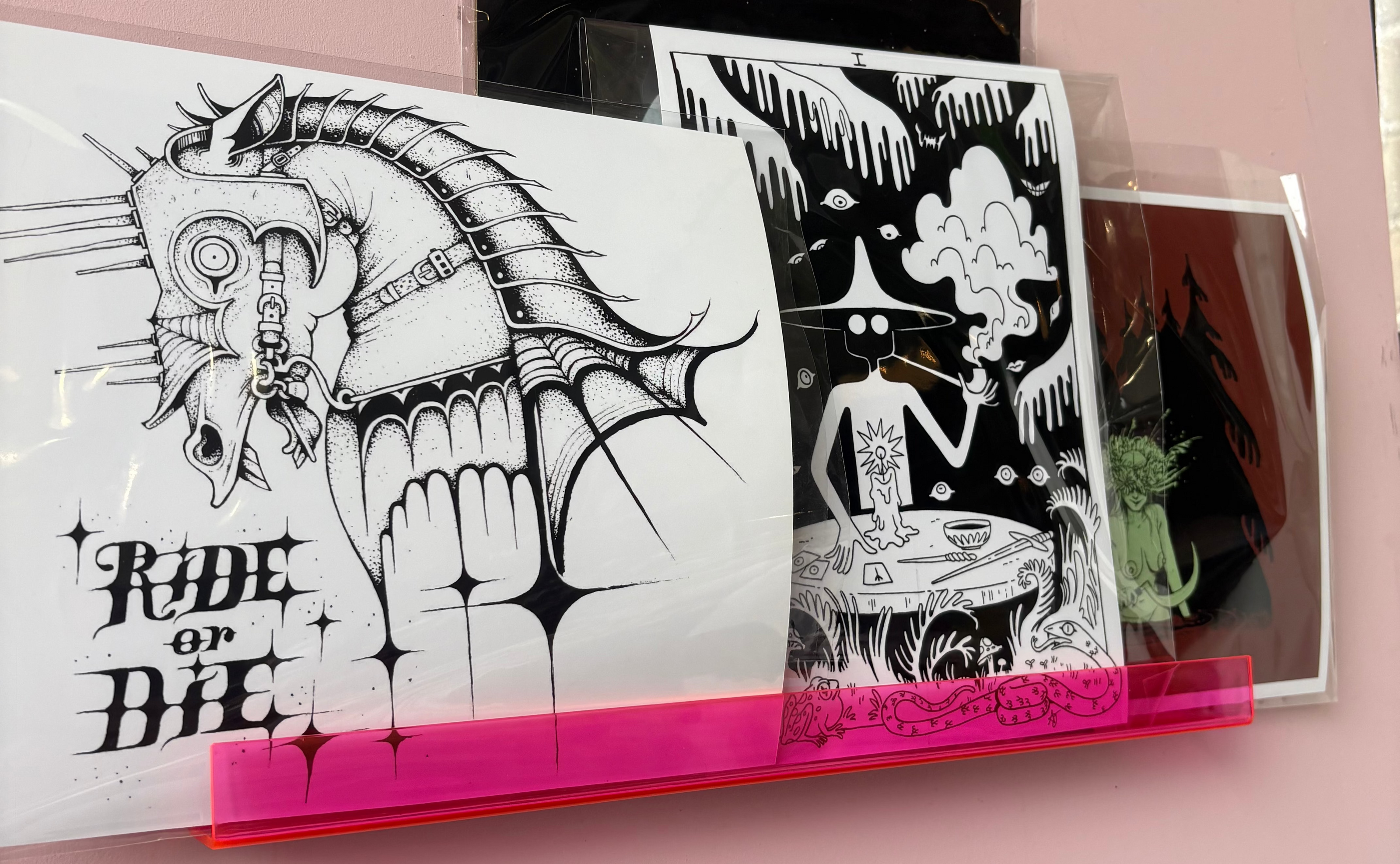 Artistic prints on a pink wall with a shelf displaying additional artwork.